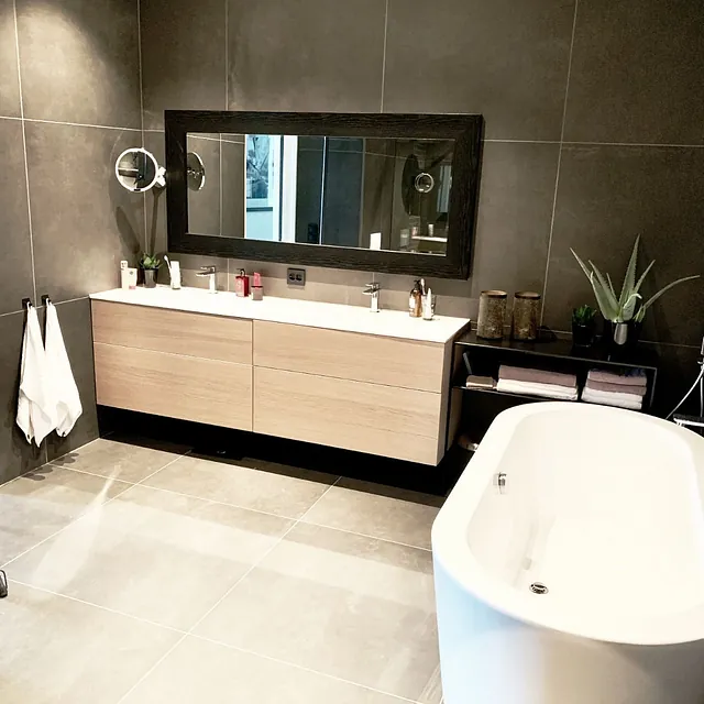 Bad med mørke fliser, frittstående badekar og lang servantbenk.