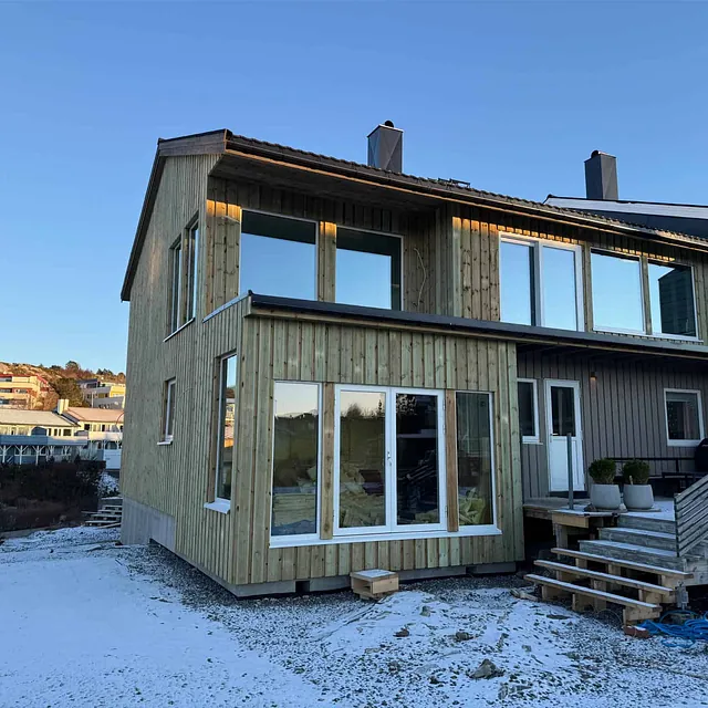 Ny enebolig med trekledning, terrasse og store vinduer i rolig boligområde.