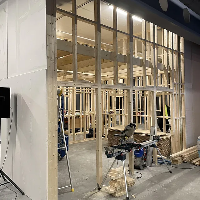 Påbegynt innvendig bygg med trestenderverk og verktøy på gulvet.