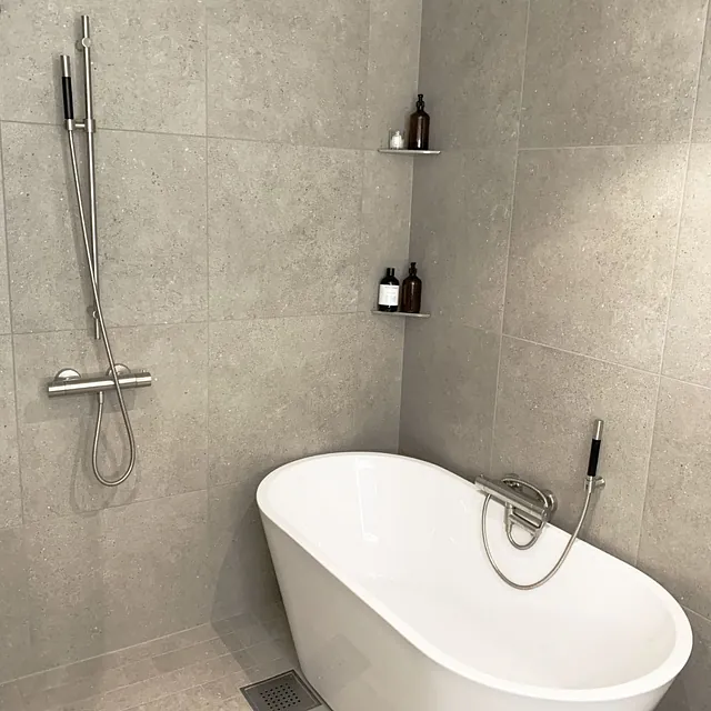 Bad med grå fliser, frittstående badekar og dusj med krom armatur.