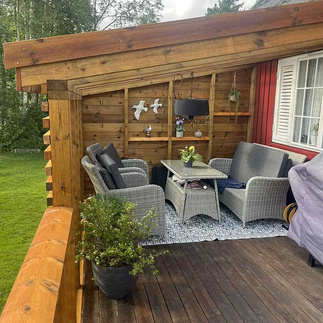 Overbygd terrasse med loungesett, bord og trevegger i lun og skjermet uteplass.