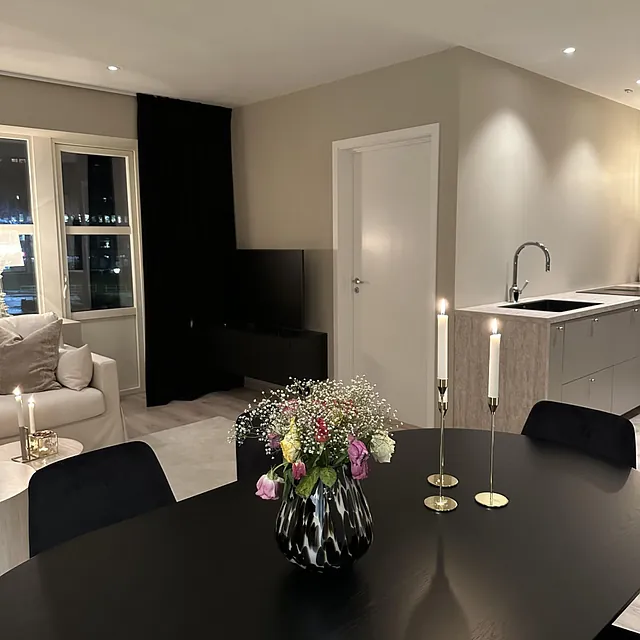 Spisestue med sort bord, blomster i vase og tente lys ved åpen stueløsning.