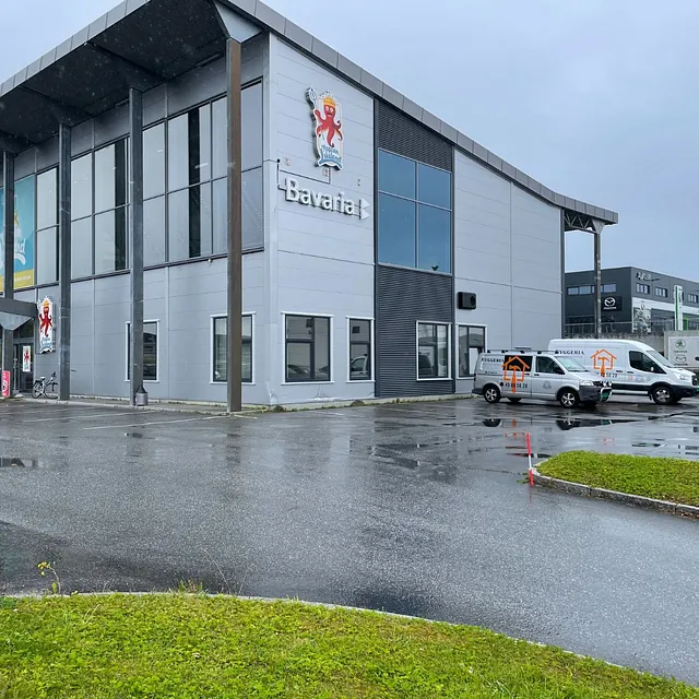 Stor grå bygning med Bavaria-skilt og varebiler parkert utenfor.