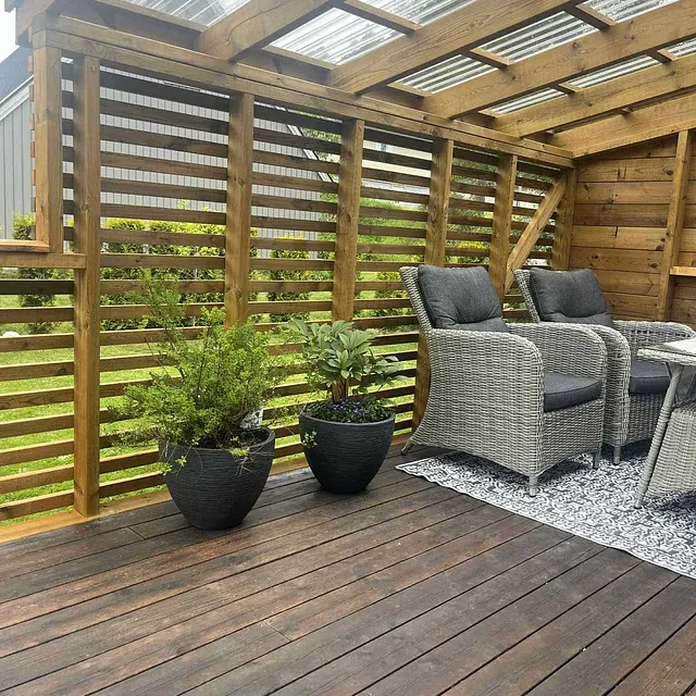 Overbygd terrasse med sittegruppe, planter og levegg i tre for skjerming ute.