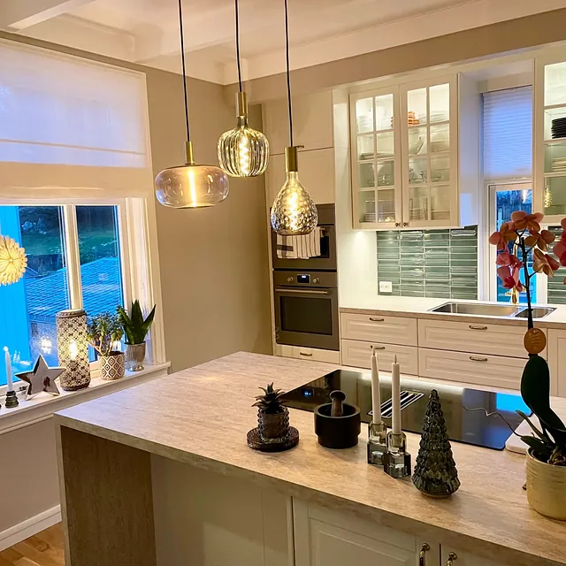 Kjøkken med hvite skap, grønne fliser og dekorative lys i vinduskarmen.