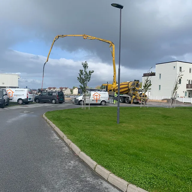 Betongbil med pumpearm i arbeid ved boligområde, firmabiler parkert ved siden.