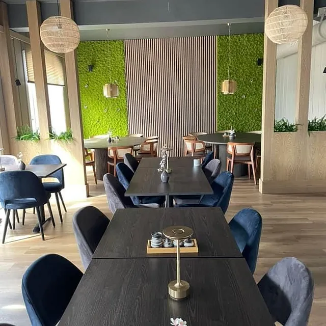 Spiseområde med grønne mosevegger, mørke bord og blå stoler.
