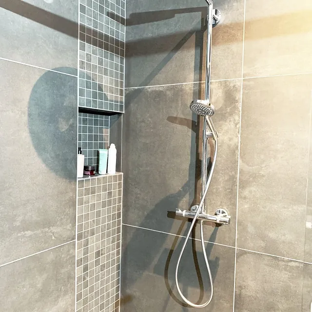 Dusj med store grå fliser, innebygde hyller og krom armatur.