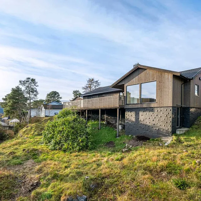 Enebolig med stor terrasse på søyler plassert i skrånende terreng med utsikt.