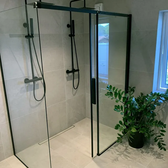 Dusjhjørne med to dusjhoder, glassvegger og store grå fliser.