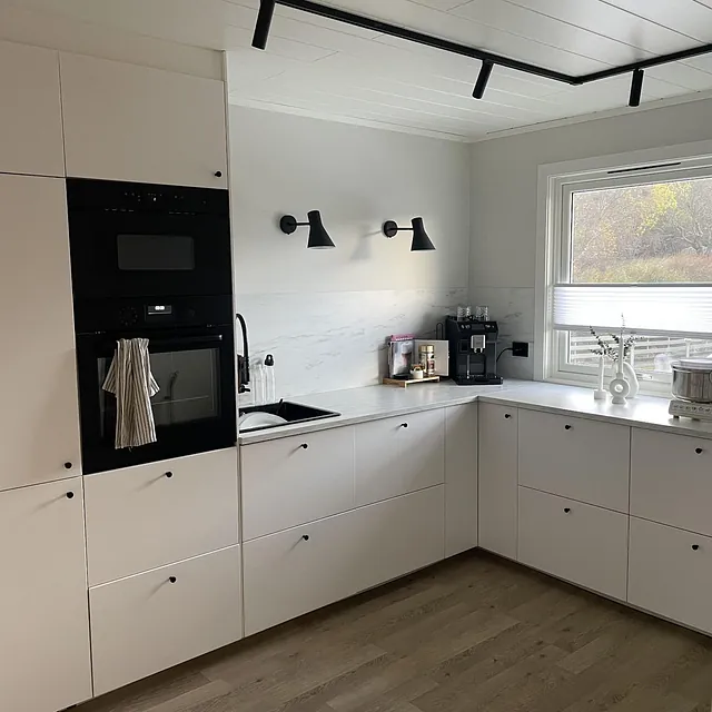 Hvitt kjøkken med integrerte hvitevarer, lyse gulv og vindu mot hagen.