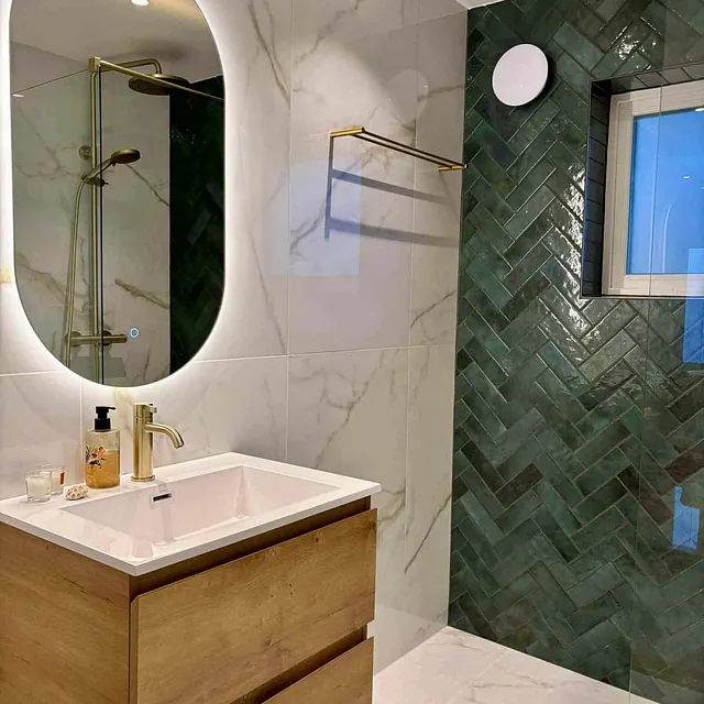 Moderne bad med servant i tre, ovalt speil og grønne fliser i dusjsone.