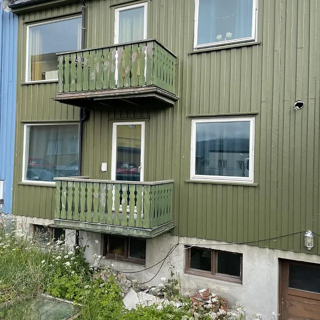 Grønn tomannsbolig med to små balkonger og hvitt betongfundament.