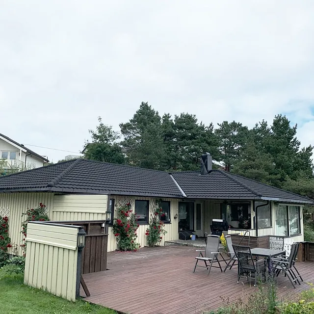 Enebolig med lys fasade, sort tak og stor terrasse med utemøbler.