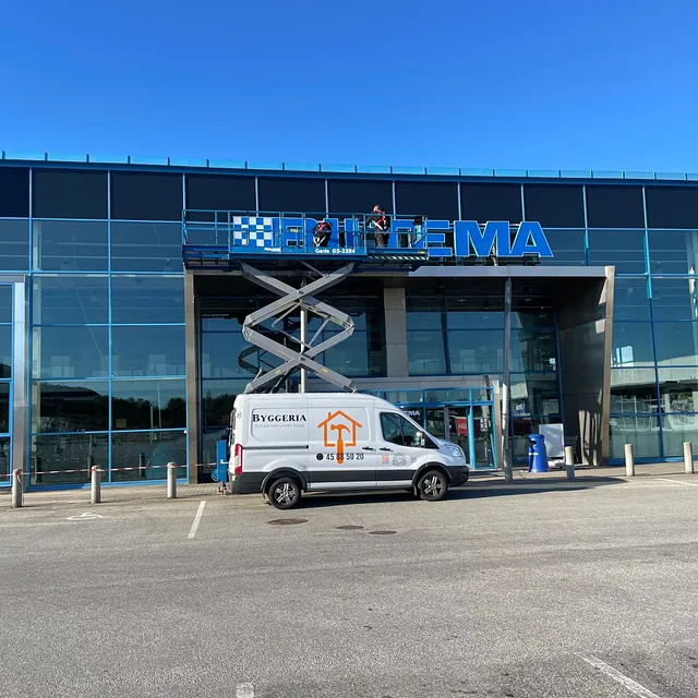 Høy lift hever arbeidere opp til stort skilt med Biltema, Thansen og JYSK.