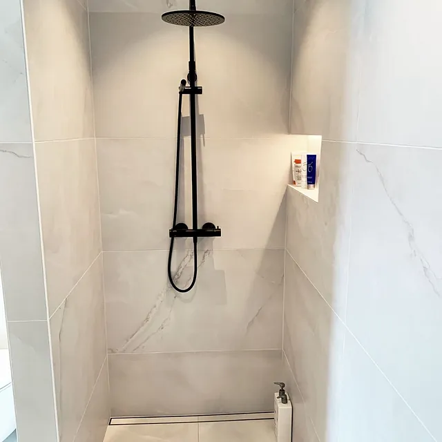 Dusjhjørne med store lyse fliser, sort armatur og nisje for såpe.