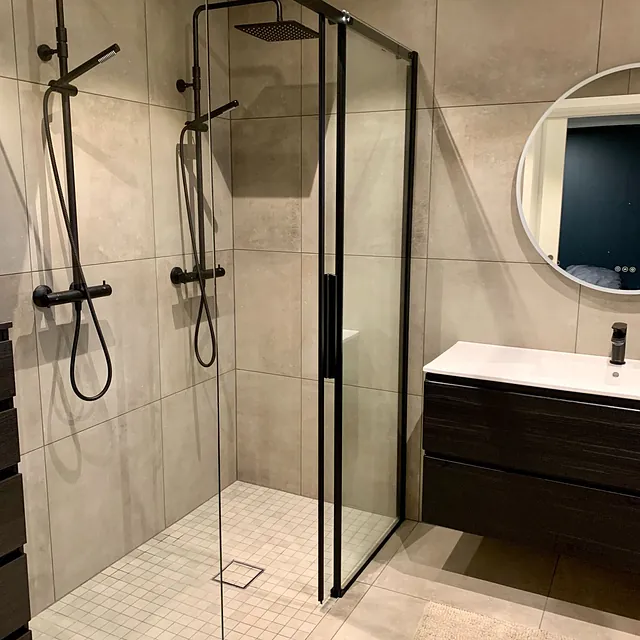 Bad med dobbeldusj i glass, store grå fliser og mørk servantinnredning.