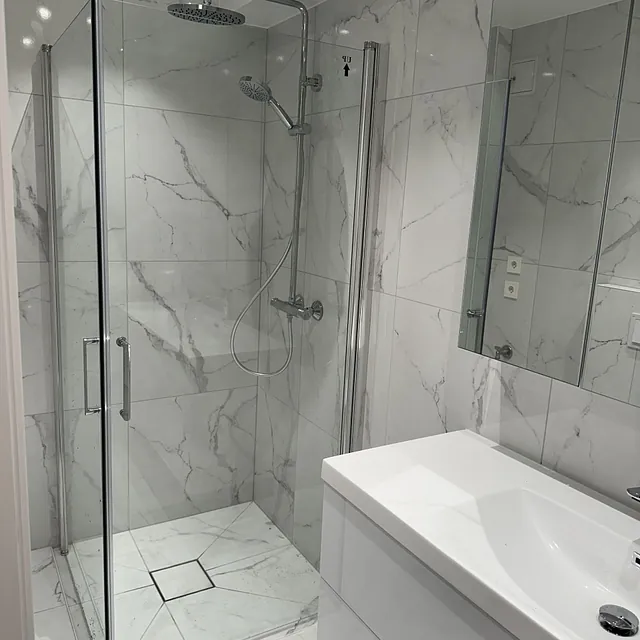 Dusjhjørne med marmorfliser, glassdør og dobbel dusjarmatur.