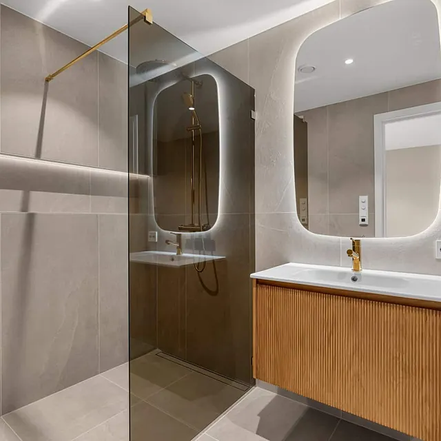 Moderne bad med dusj, servant i tre og speil med integrert belysning på vegg.