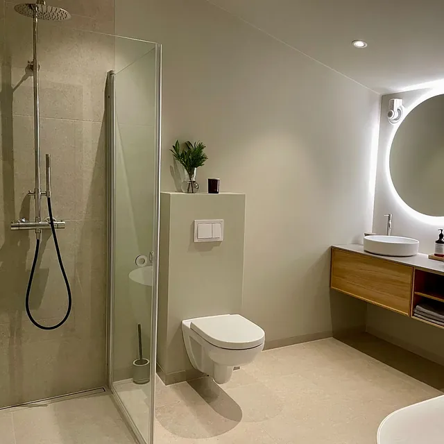 Moderne bad med dusj, vegghengt toalett, servant med treinnredning og opplyst speil.