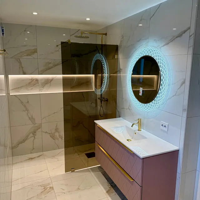 Stilrent bad med dusj bak glassvegg, servant og speil med dekorativ belysning.