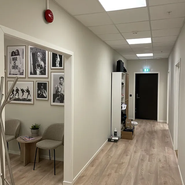 Gang med tredekor, veggbilder og lite sittehjørne med stoler.