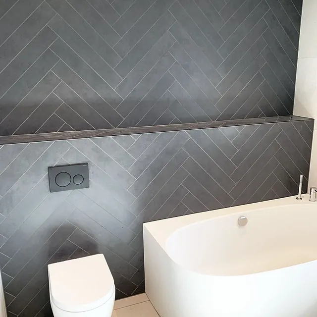 Bad med mørk fiskebeinsflis, frittstående badekar og vegghengt toalett.