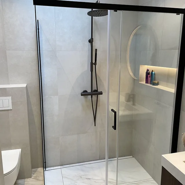 Bad med dusjkabinett, store fliser, nisjehyller og sort dusjarmatur.