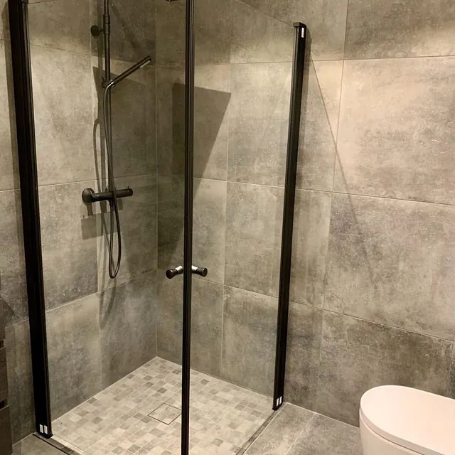 Bad med mørkegrå fliser, dusj med glassvegger og sort dusjarmatur.