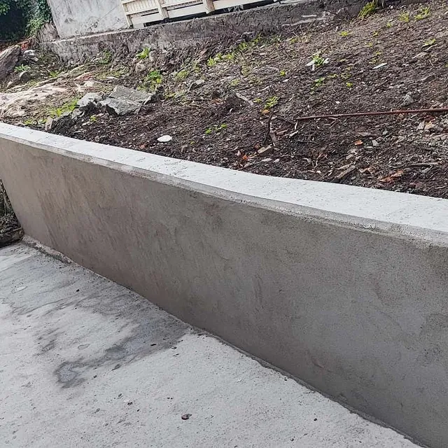 Nystøpt betongmur langs skråning ved enebolig med uteplass.