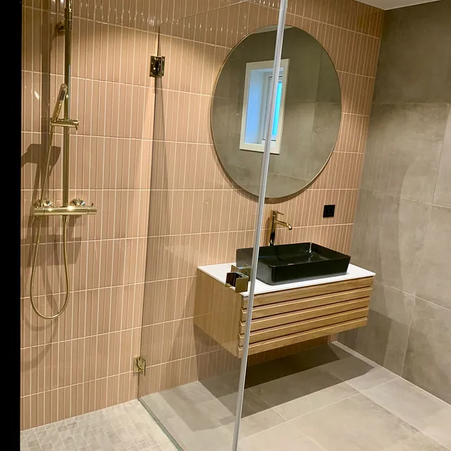 Bad med oransje fliser, sort servant, rundt speil og gullfarget dusjarmatur.