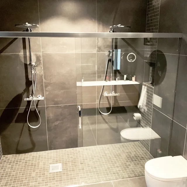 Bad med mørke fliser, dobbel dusj og glassvegg.