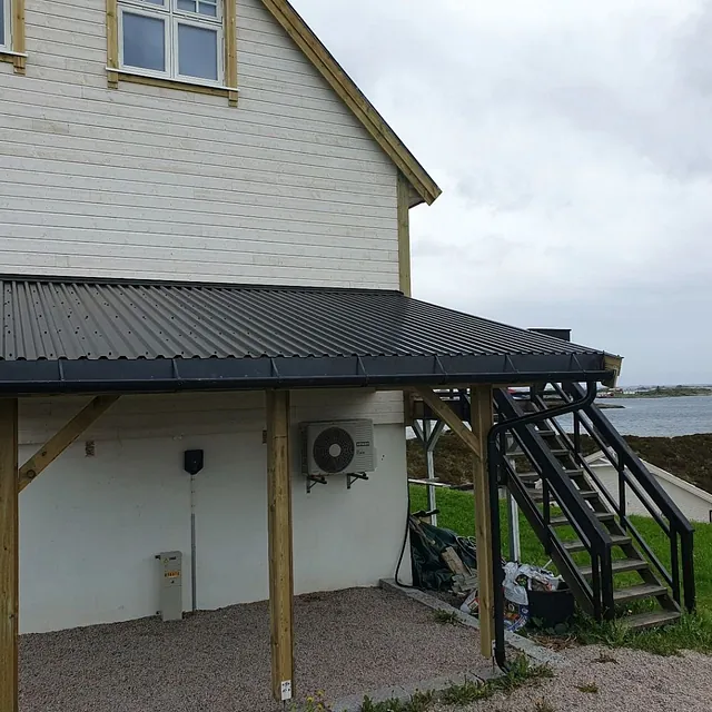Påbygg med sort takplater og utvendig trapp i metall ved hvitt hus.