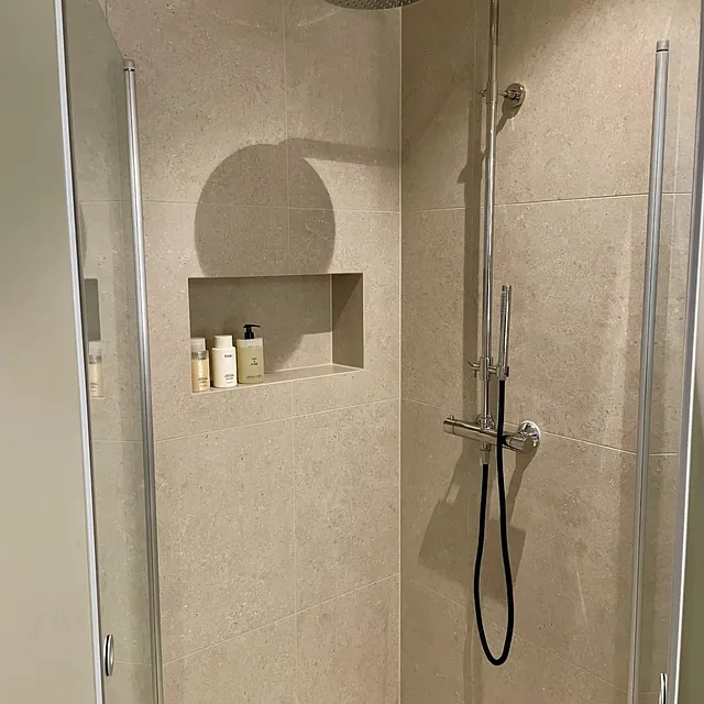 Dusj med beige fliser, nisje og regndusj i krom.