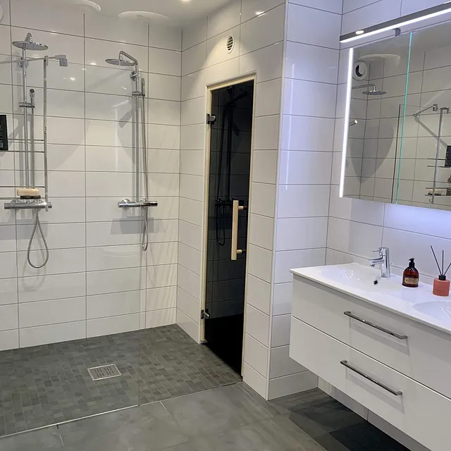 Bad med store grå gulvfliser, mørk servant med doble vasker og stort speil.