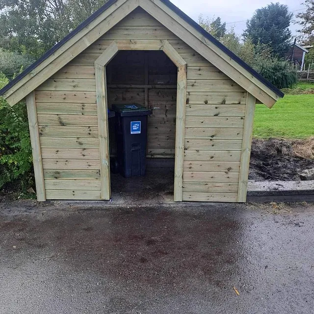 Liten bod i tre med svart tak, brukt som oppbevaring av søppelkasser.