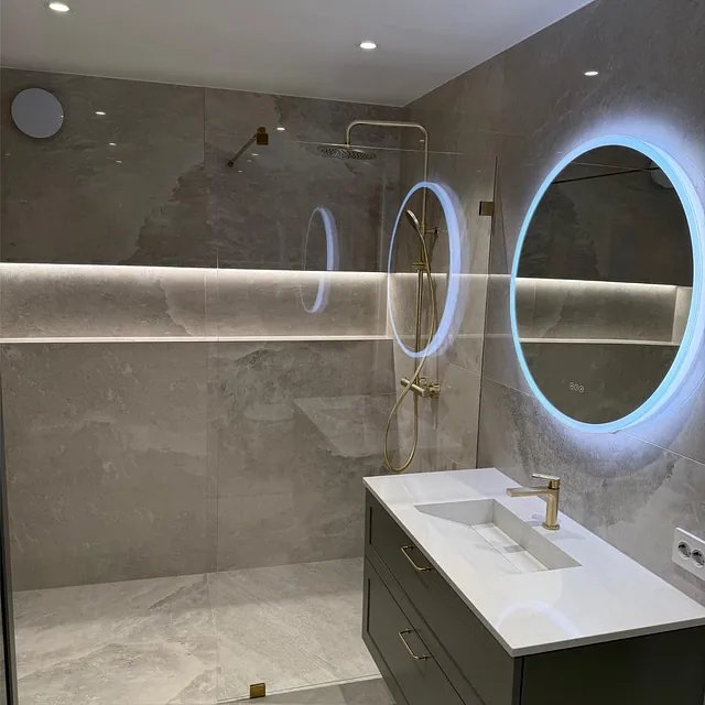 Moderne bad med dusj, servant og rundt speil med integrert lys på vegg.