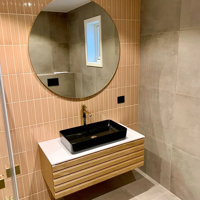 Bad med oransje fliser, rundt speil, sort servant og treinnredning.