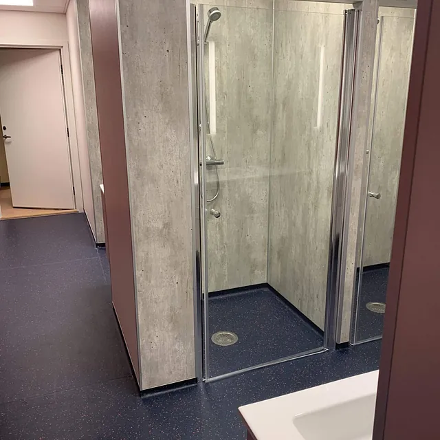 Garderobeområde med dusjkabinett, grå veggplater og mørk blått gulv.