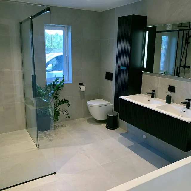 Romslig bad med dusjhjørne, dobbel servant i svart og store grå fliser.