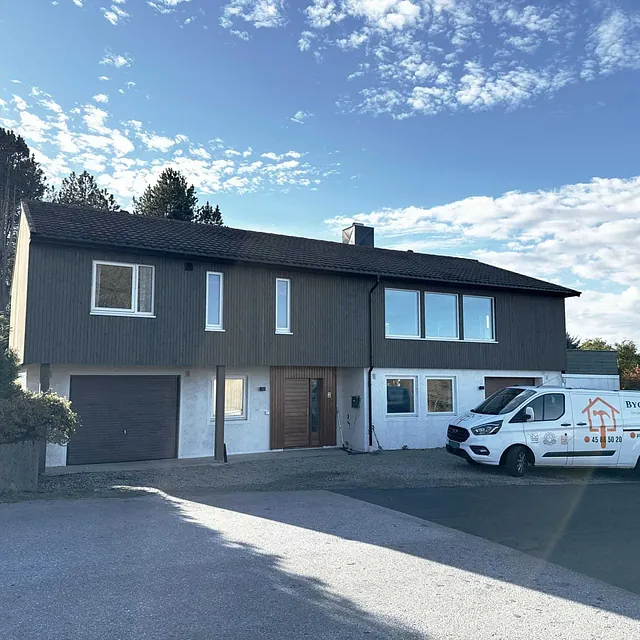 Moderne enebolig med garasje og firmabil parkert foran hus i solrikt boligområde.