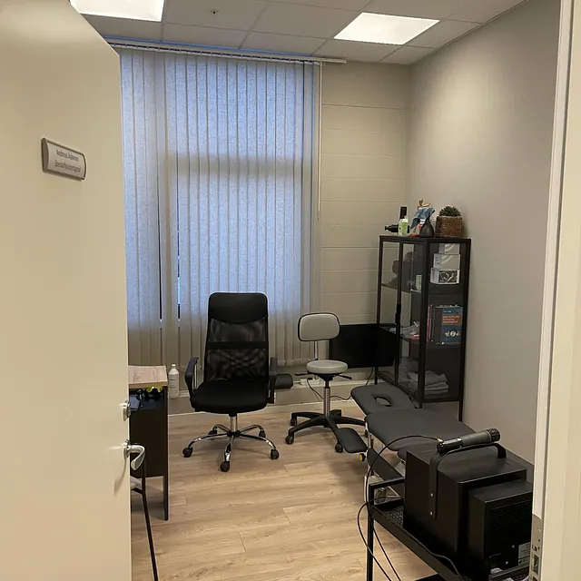 Kontor med skrivepult, kontorstoler og behandlingsbenk ved vindu.