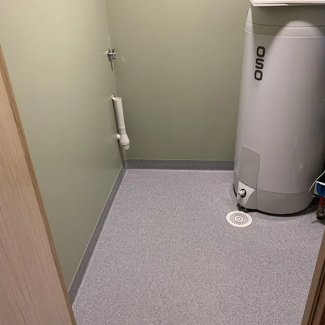 Lite rom med grønnmalte vegger, grå gulvbelegg og varmtvannsbereder.