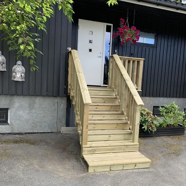 Svart hus med ny tretrapp og gelender ved hvit inngangsdør.