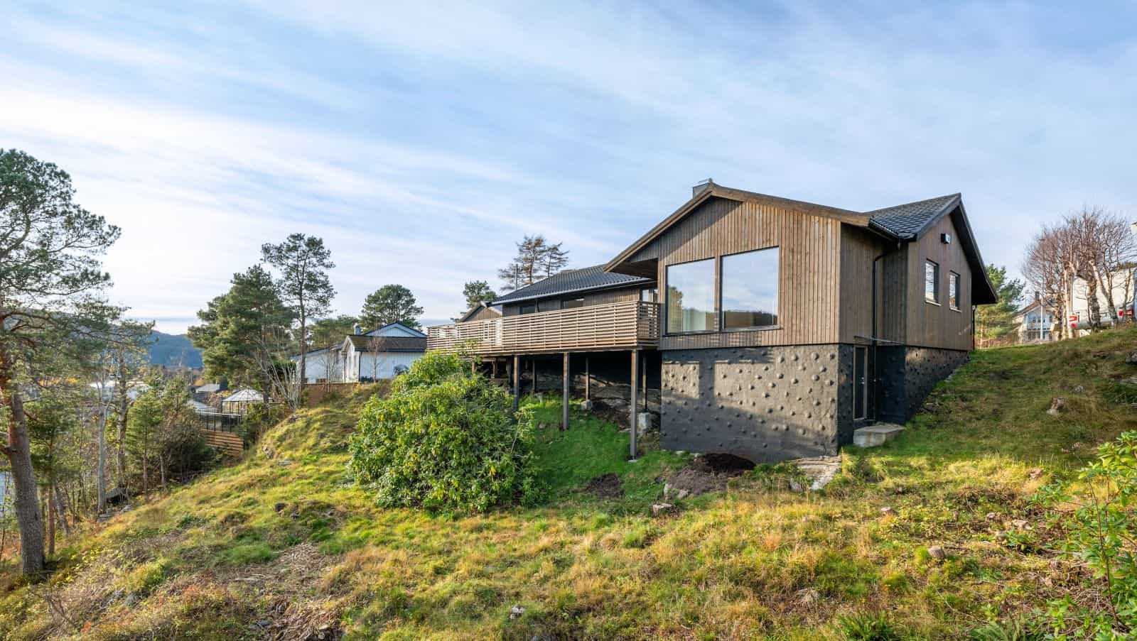 Enebolig med stor terrasse på søyler plassert i skrånende terreng med utsikt.
