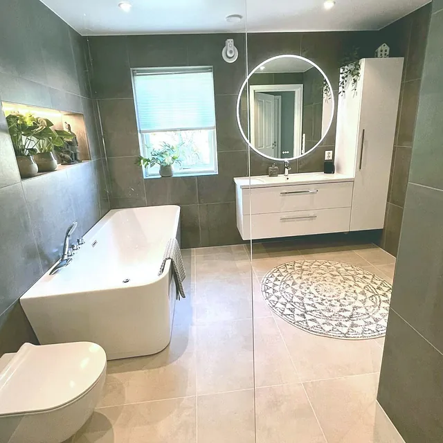 Moderne bad med badekar, hvit servant, rundt speil og grønne planter.