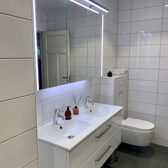 Bad med hvite fliser, dobbelt servant, stort speil og vegghengt toalett.