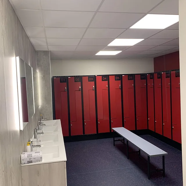 Moderne garderoberom med røde skap, hvite vasker, speil og benk i midten.