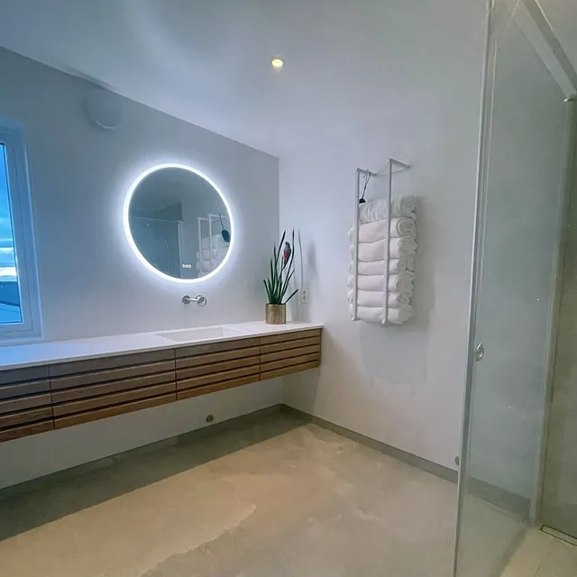 Lyst bad med treinnredning, rundt opplyst speil og utsikt fra vindu.