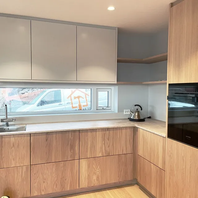 Kjøkken med tre- og gråfronter, lang horisontal vindu og integrerte hvitevarer.